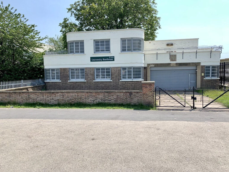 A white, two-story building with a flat roof and numerous windows. It has a brick wall in front and a large garage-style door on the right side, with a black metal gate leading to the entrance. The building is undergoing refurbishment by Allsopp Construction.