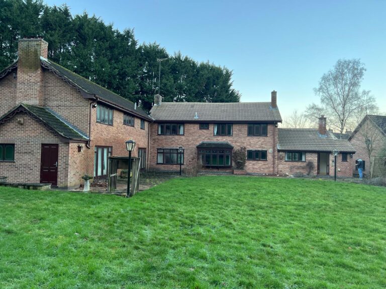 Allsopp Construction's extension and renovation project; Woodlands, Draycott in the Clay, Staffordshire in 2021 before the renovation began. Rear view of the L-shaped red brick large home with brown windows and lawn area in front.