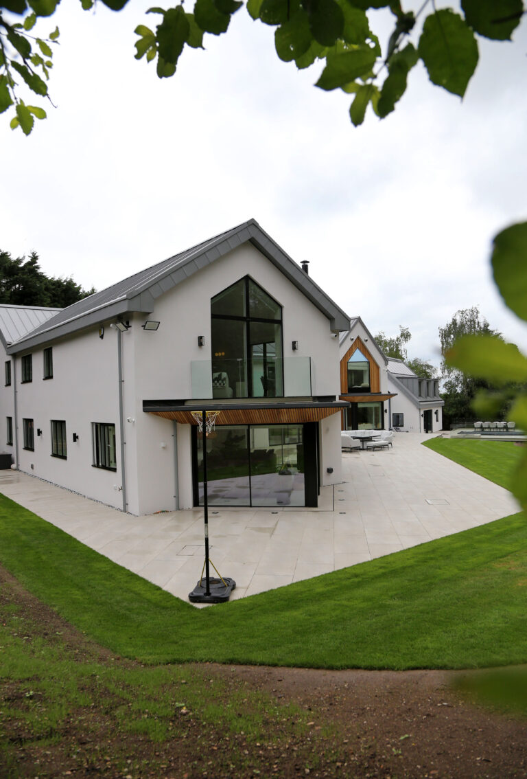 Rear elevation of Woodlands in Draycott in the Clay. White gable end with large triangular window and standing seam aluminium roof.