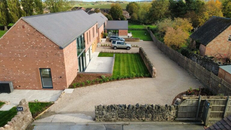 Two new dwellings in Breedon on the Hill, Leicestershire. Houses are linear, brick buildings with slate roofs and large anthracite glazing.