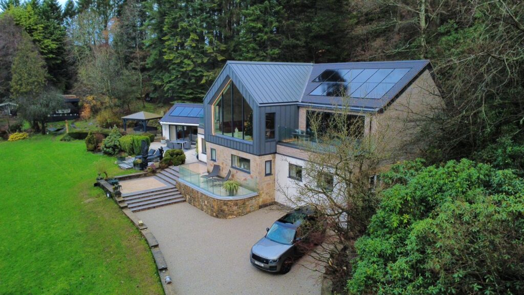 Large detached house with grey aluminum roof, solar panels and large front window a renovation project by Allsopp Construction. Sweeping driveway and gardens to the front.