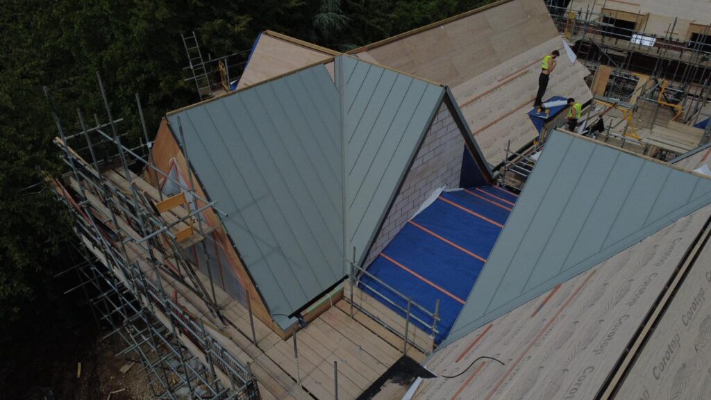 Aerial drone photograph of Plot 3 at The Paddocks in Bradmore, Nottingham, showing the roof structure under construction, including the central glazed atrium and standing seam roof sections.