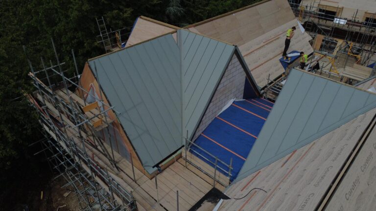 Aerial drone photograph of Plot 3 at The Paddocks in Bradmore, Nottingham, showing the roof structure under construction, including the central glazed atrium and standing seam roof sections.