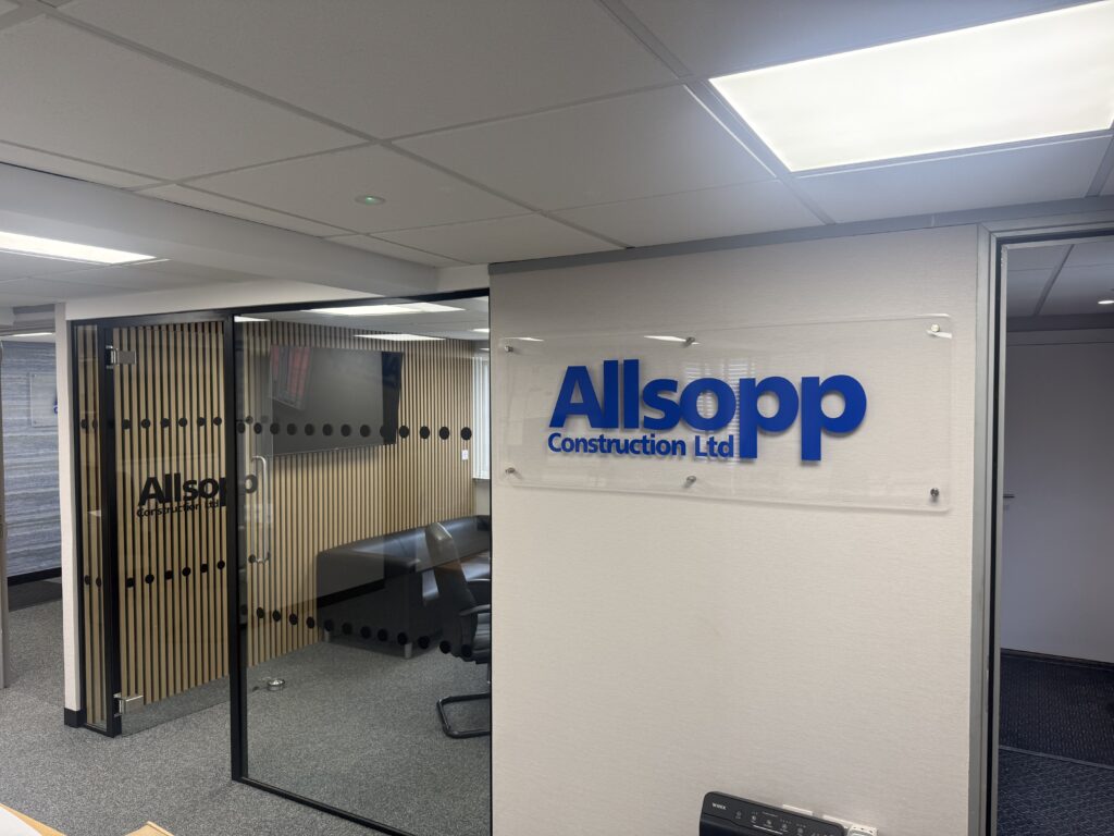 Interior of Allsopp Construction new offices. Showing Allsopp Construction blue sign and crittal style glass doors into the meetng room with black chairs and a table.