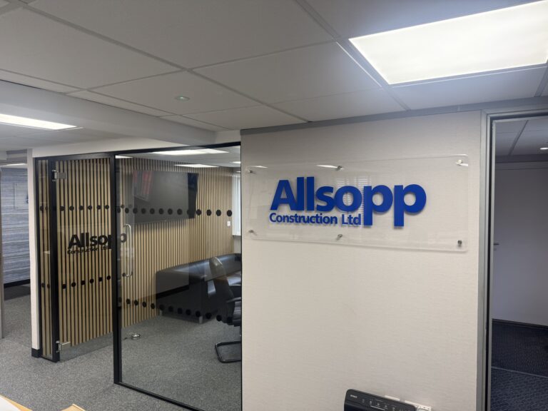 Interior of Allsopp Construction new offices. Showing Allsopp Construction blue sign and crittal style glass doors into the meetng room with black chairs and a table.