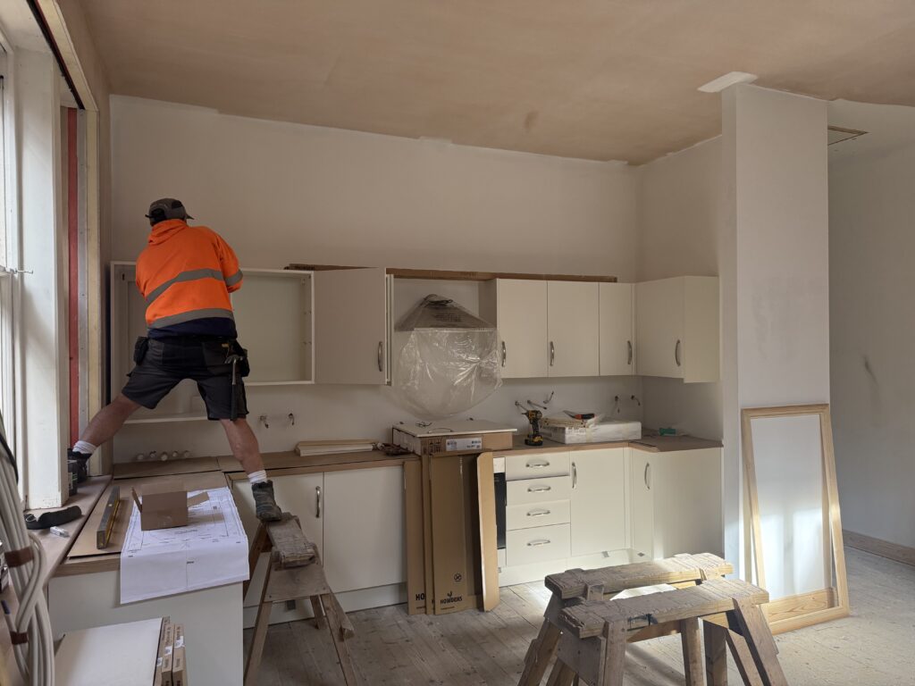 Liversage Trust Almshouses Refurbishment Project kitchen being installed. Cream called kitchen units beng fitted on to a new plastered wall.