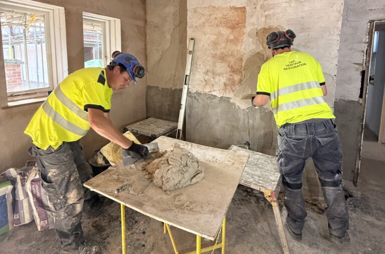 The Liversage Trust Almshouses refurbishment, two men in hi-vis tops lime pastering the old original walls.